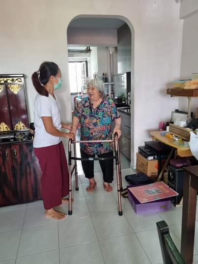Helper assisting an elderly person using a walker at home